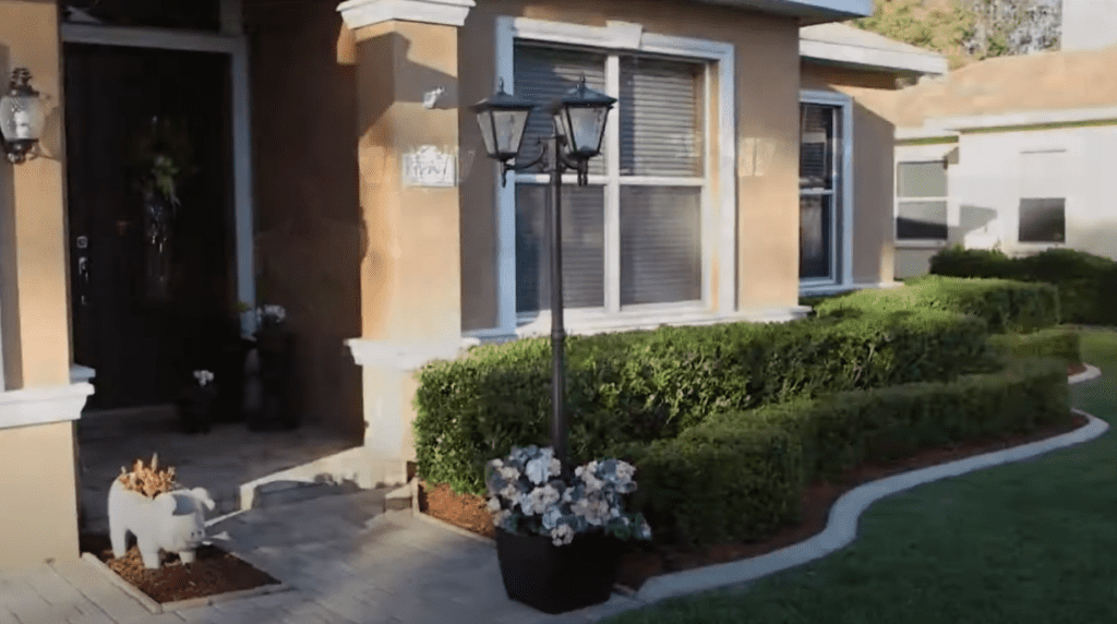 A 3 light solar lamp post that has a planter filled with flowers outside of a home - techgoodandbad.com